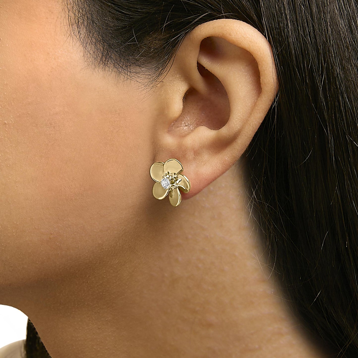 Close-up side view of a model wearing a yellow metal flower-shaped earring with a round white gemstone in the center.
