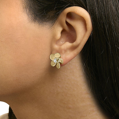 Close-up side view of a model wearing a yellow metal flower-shaped earring with a round white gemstone in the center.
