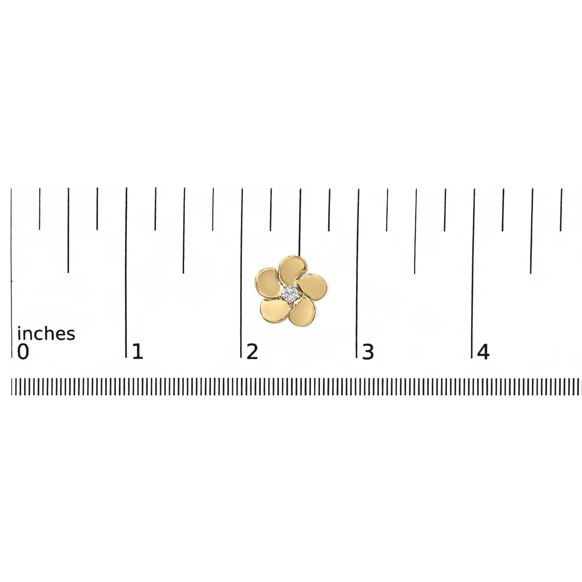 Close-up top view of a small yellow metal flower-shaped earring with a single white round gemstone in the center, shown placed on a ruler scale.