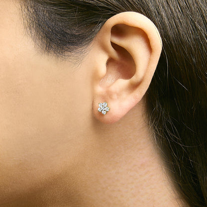 Yellow metal earrings with round white gemstones in a prong setting arranged in a floral cluster, shown worn on a model's ear in a close-up side view.