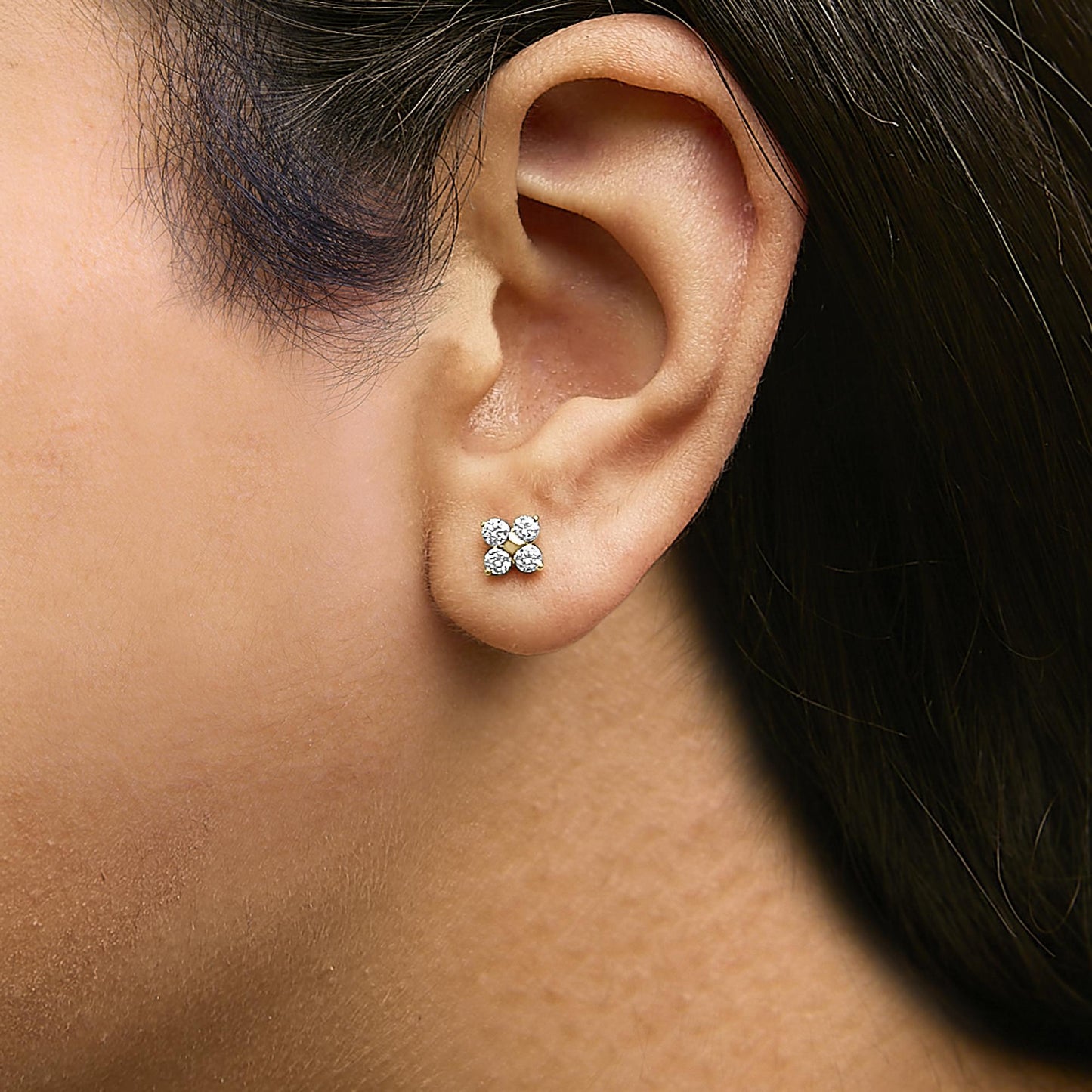 Close-up side view of a model wearing yellow metal stud earrings with four round white gemstones in prong settings.