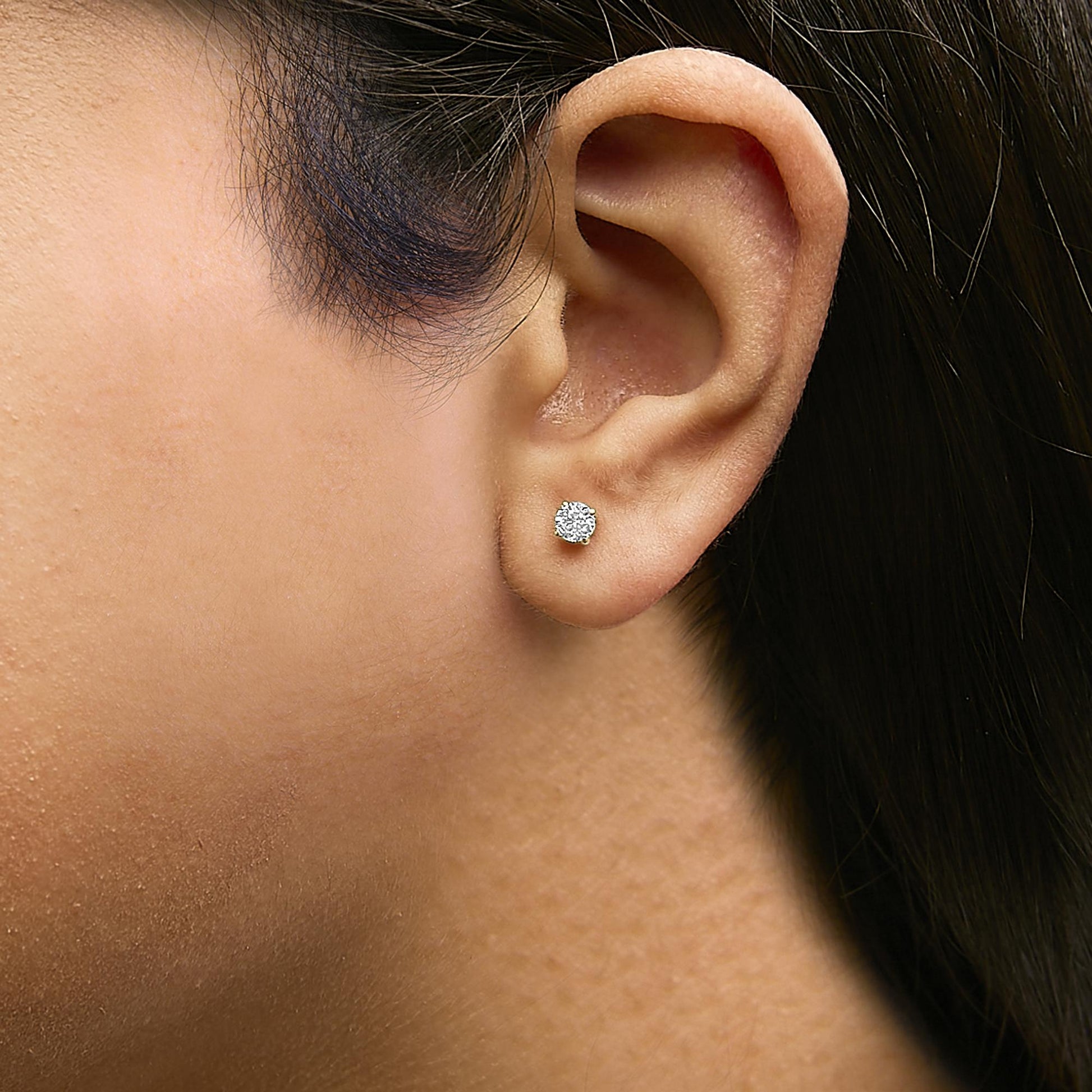 Close-up side view of a model wearing a yellow metal stud earring featuring a round white gemstone held in a 4-prong setting.