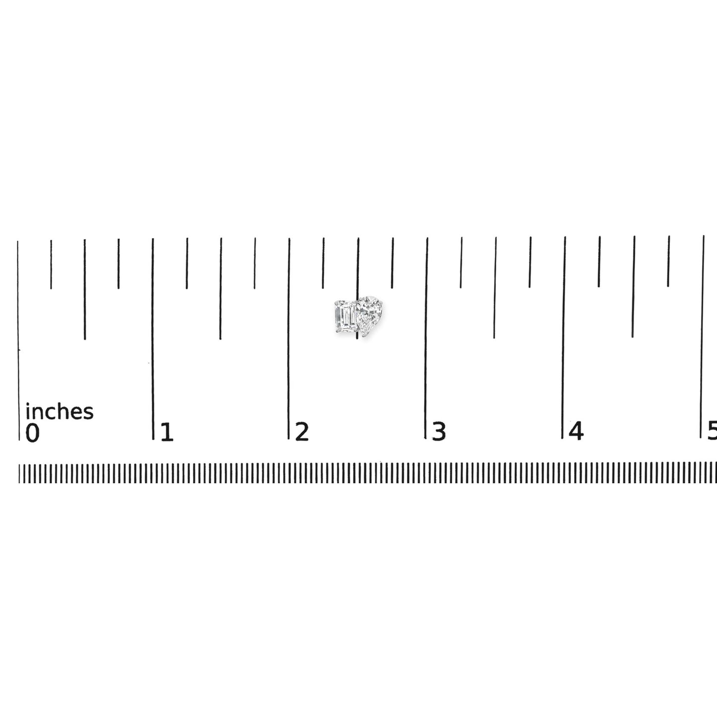 White metal earrings with one emerald-shaped white gemstone in four-prong setting and one pear-shaped white gemstone in three-prong setting, shown on a ruler for scale from a top-front angle.