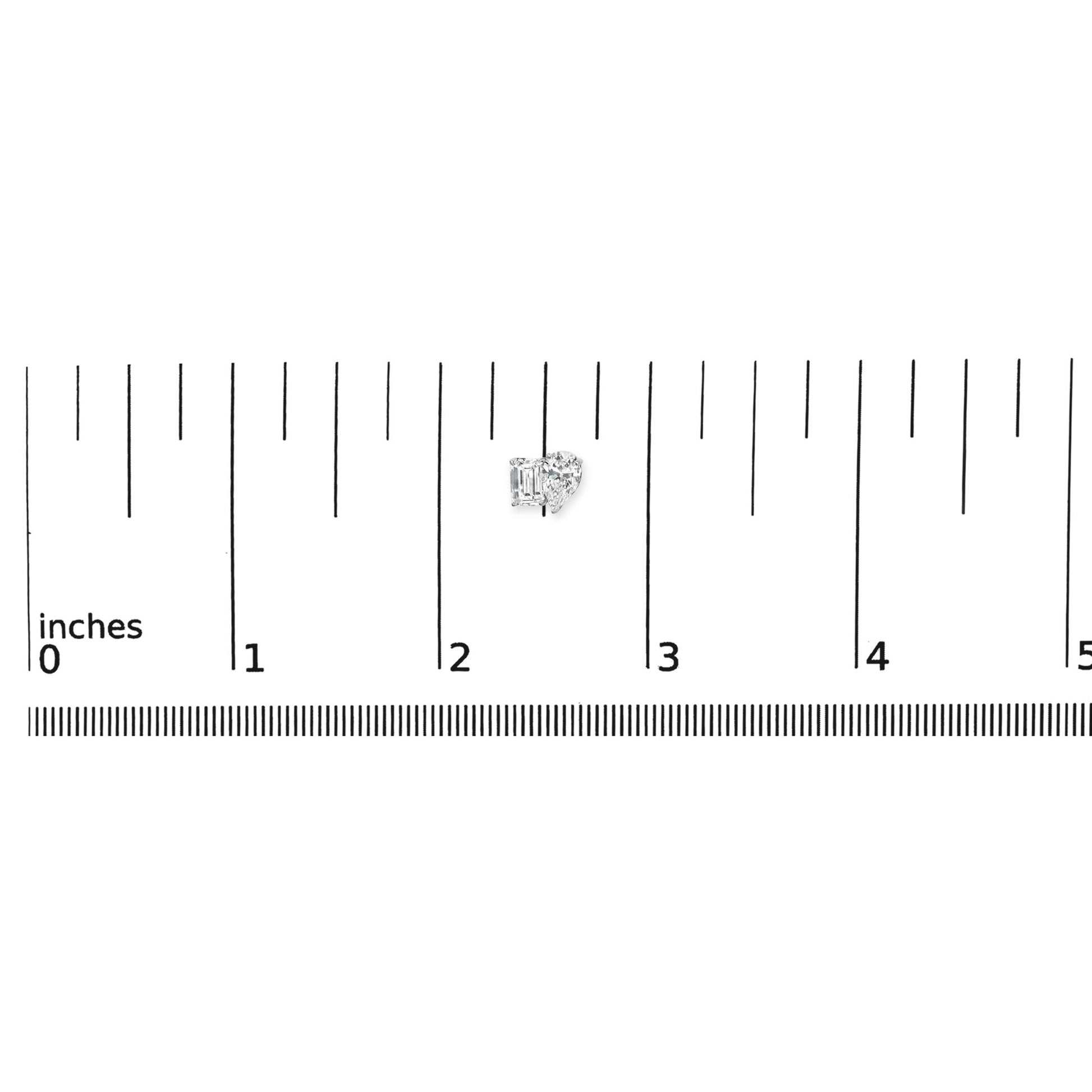 White metal earrings with one emerald-shaped white gemstone in four-prong setting and one pear-shaped white gemstone in three-prong setting, shown on a ruler for scale from a top-front angle.