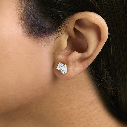 Close-up side view of a model wearing yellow metal earrings featuring one white gemstone in an emerald shape with a four-prong setting and one white gemstone in a pear shape with a three-prong setting.