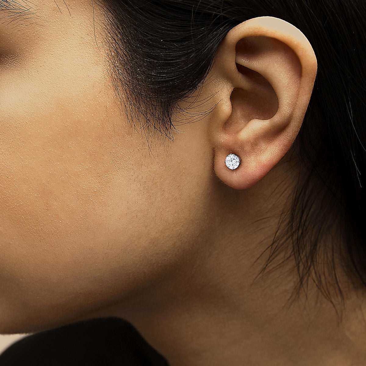 Close-up side view of a model wearing white metal stud earrings with round white gemstones set in four-prong settings.