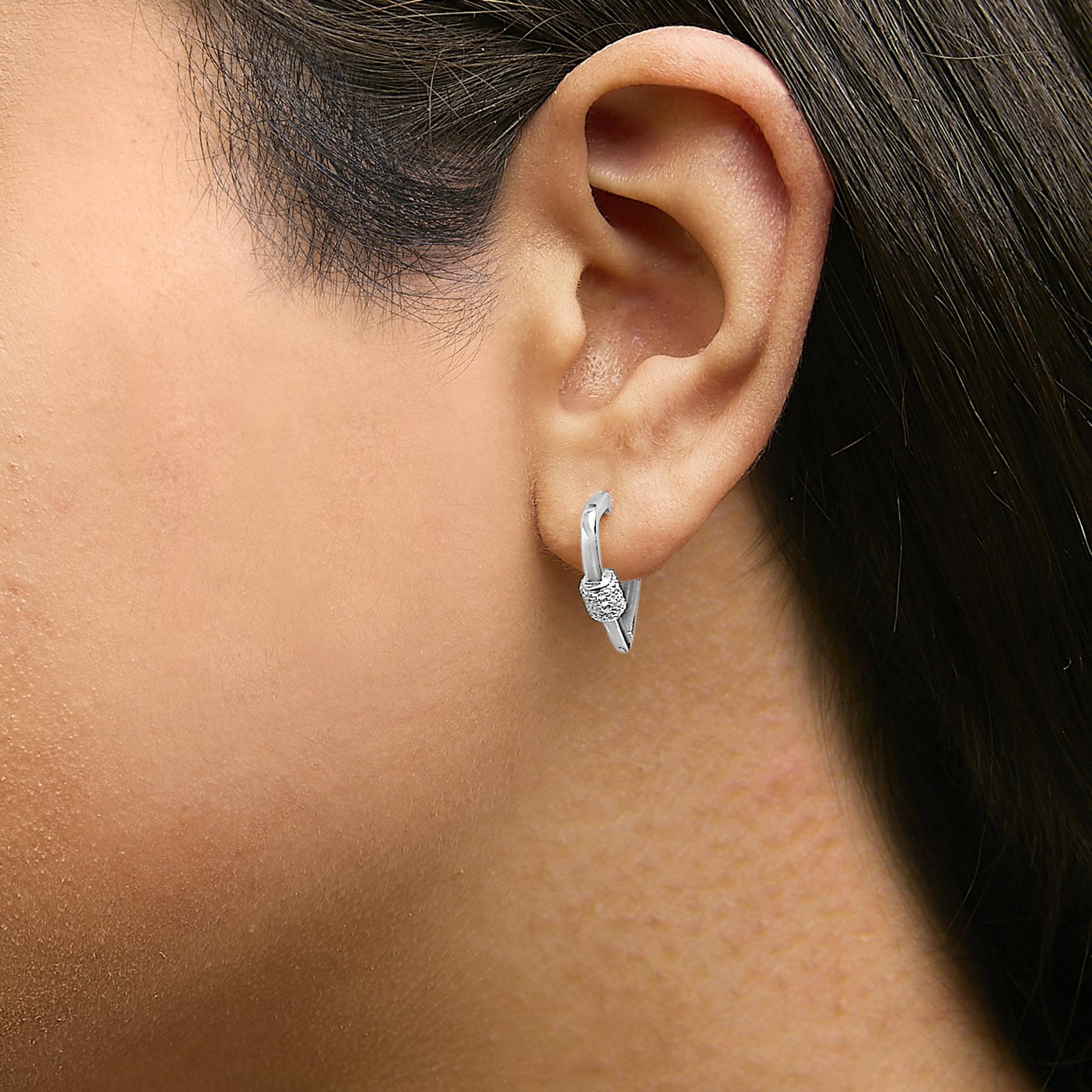 Close-up side view of a model wearing white metal hoop earrings with a cluster of small round white gemstones in a shared prong setting.