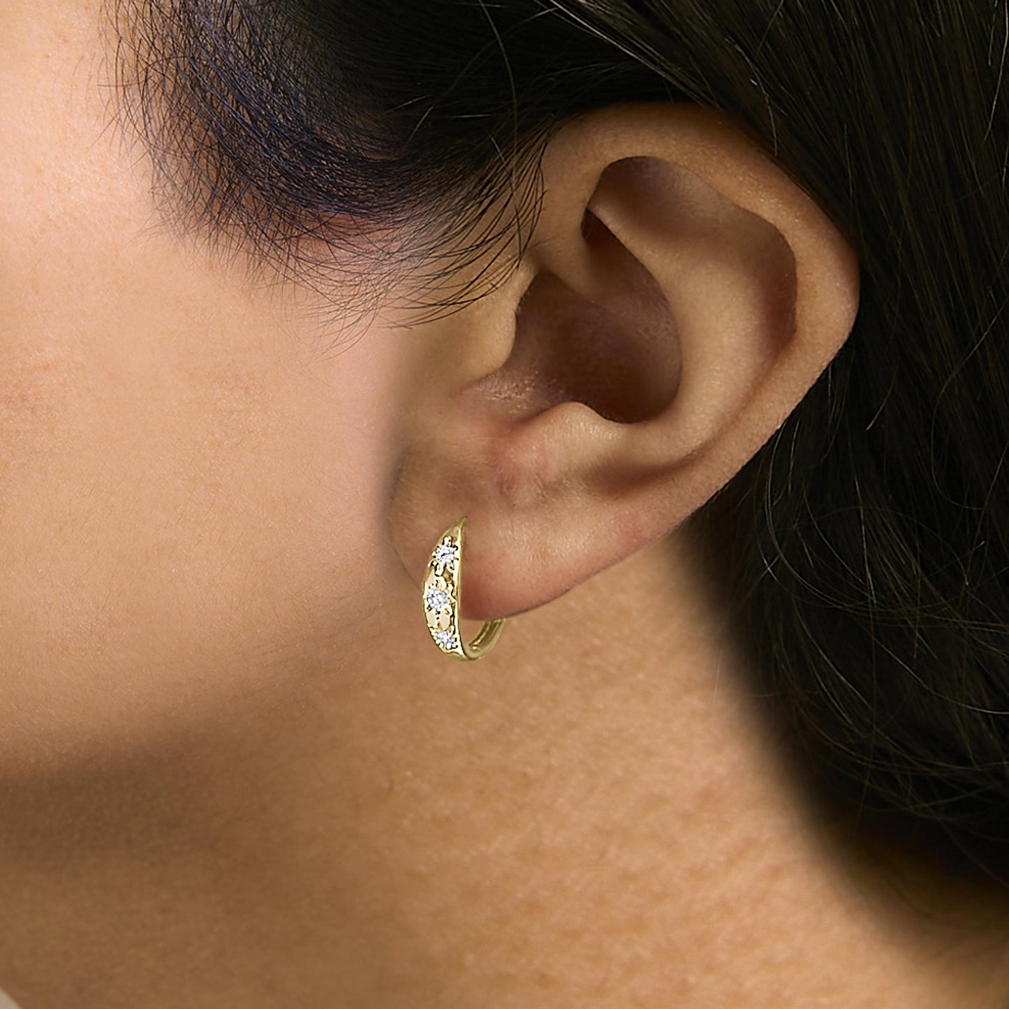 Close-up side view of a model wearing a yellow metal earring with a curved design featuring round white gemstones in prong settings.