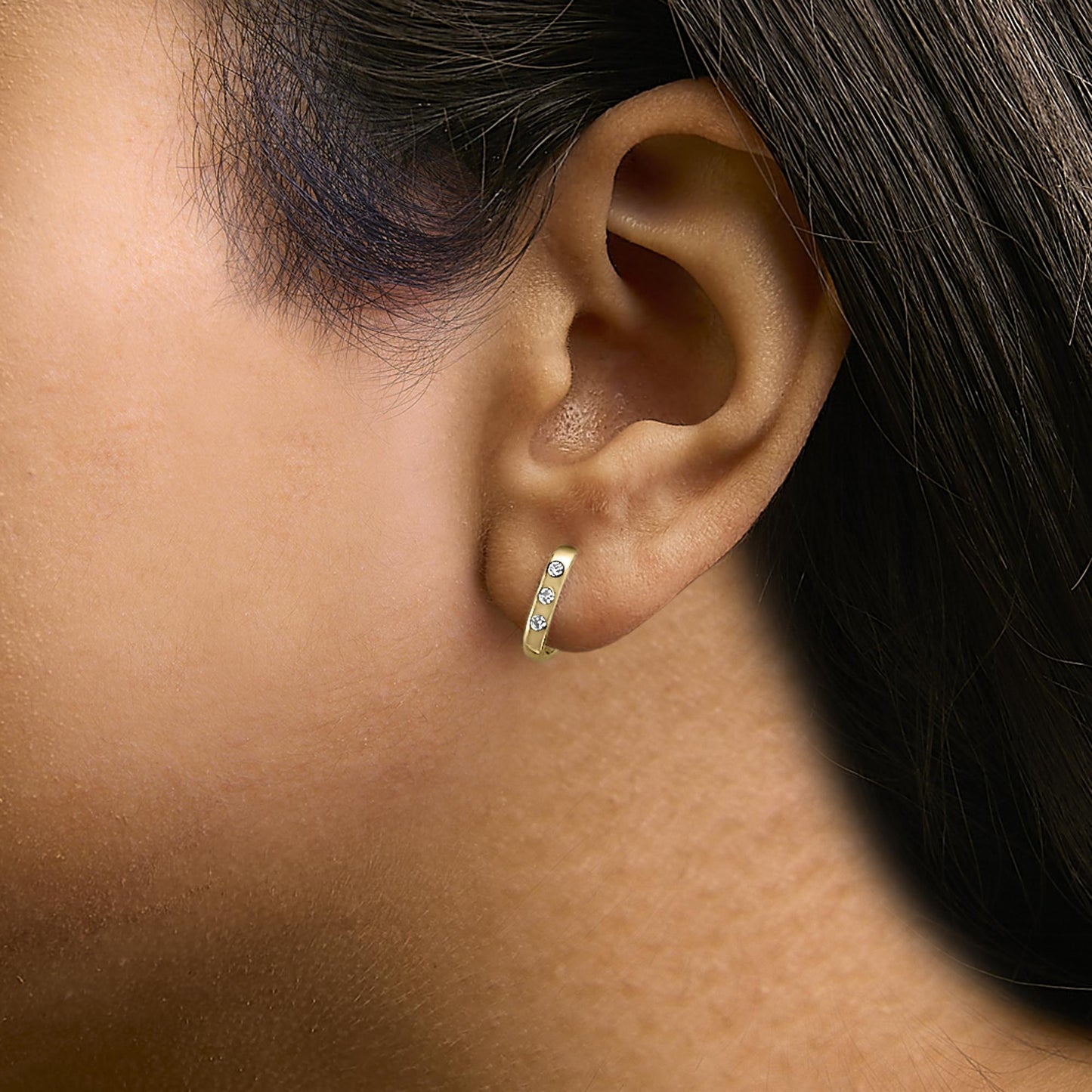 Close-up side view of a model wearing a yellow metal hoop earring with three white round gemstones in bezel settings along the front.