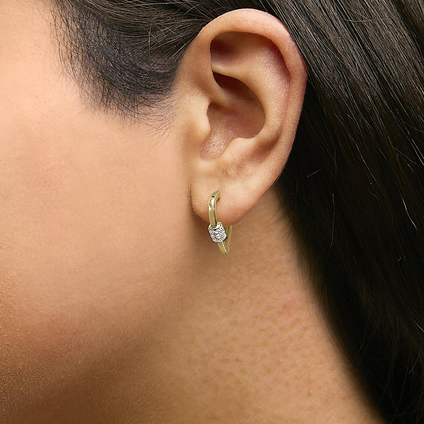 Close-up side view of a yellow metal hoop earring with cluster of round white gemstones in shared prong setting, shown worn on a model.