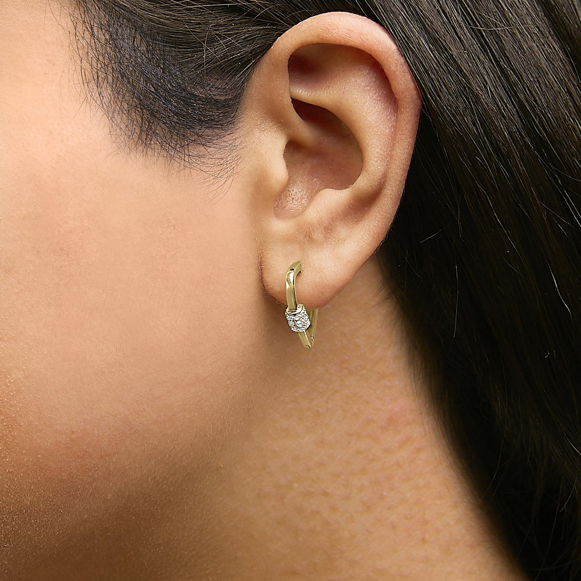 Close-up side view of a yellow metal hoop earring with cluster of round white gemstones in shared prong setting, shown worn on a model.