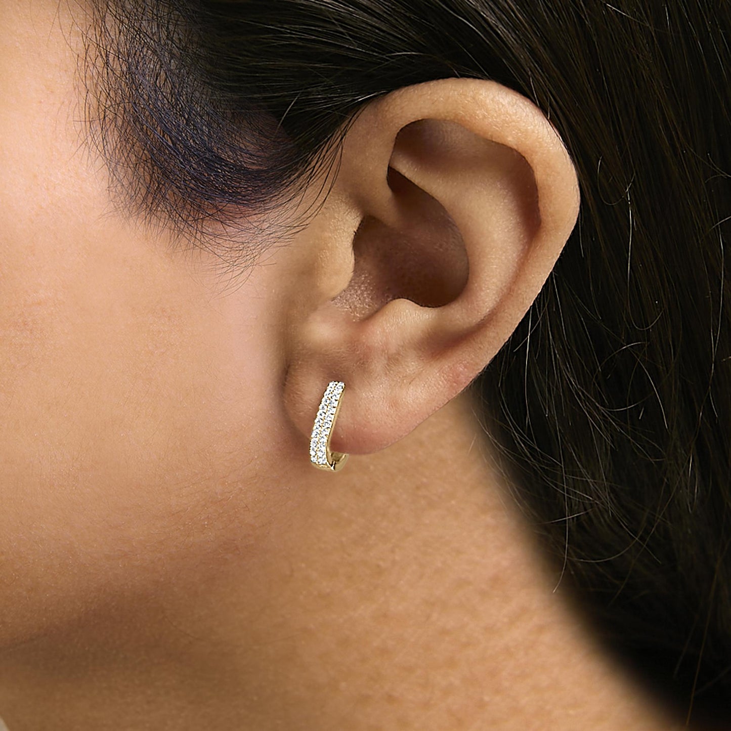 Close-up side angle of a model wearing a yellow-colored small hoop earring with two rows of round white gemstones in shared prong setting.