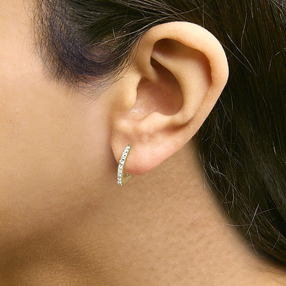 Close-up side view of a yellow metal earring with a curved row of small white round gemstones, shown worn on a model's ear.