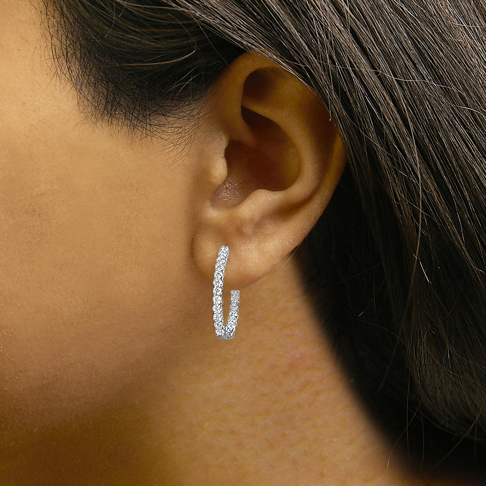 Close-up side view of a model wearing white metal hoop earrings adorned with round white gemstones in a shared prong setting.