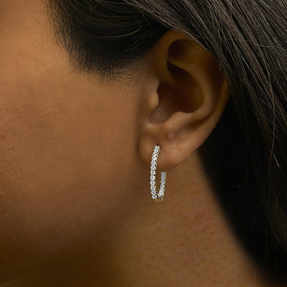 Close-up side view of a model wearing a yellow metal hoop earring adorned with round white gemstones set in a shared prong setting.