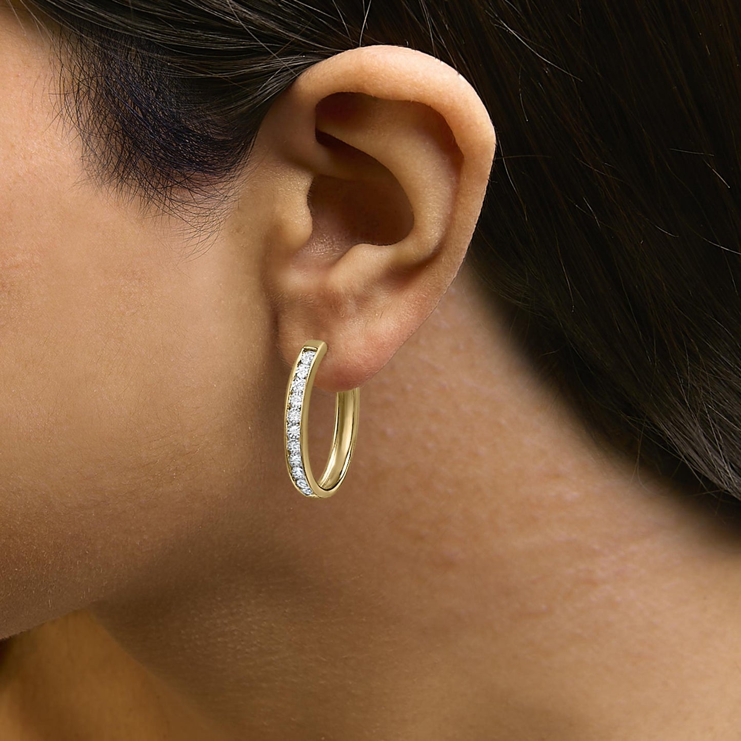 Close-up side view of a model wearing a yellow and white metal hoop earring set with round white gemstones in a bezel setting along the front outer edge.