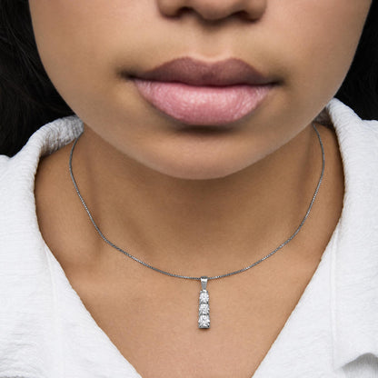 Close-up front view of a white metal necklace with a pendant featuring three round white gemstones in a channel setting, shown worn on a model.