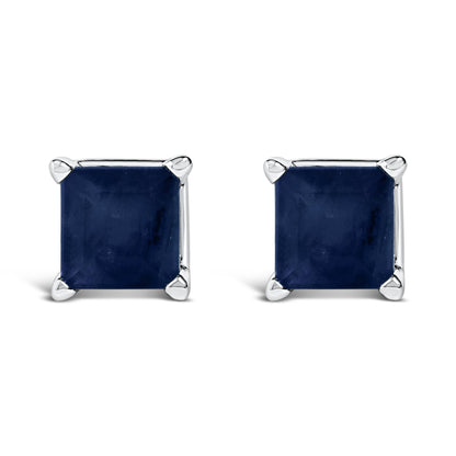 Front angled view of white metal stud earrings featuring square blue gemstones set in four-prong settings.