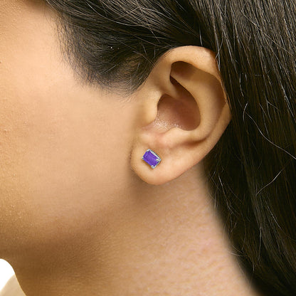 Close-up side view of a model wearing a white metal stud earring with a purple emerald-shaped gemstone held by a 4-prong setting.