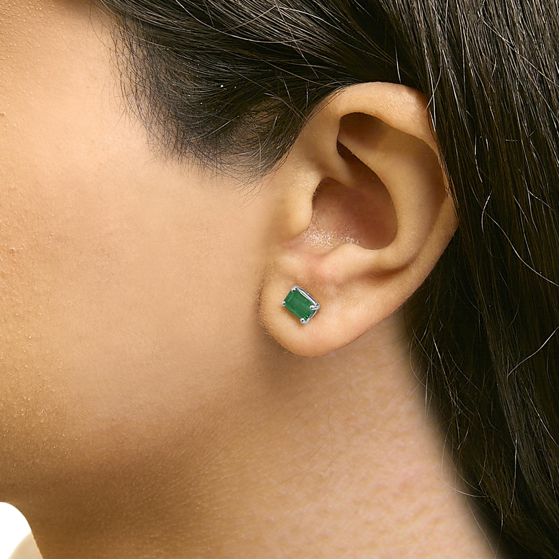 Close-up side view of a model wearing white metal stud earrings with rectangular green gemstones set in four-prong settings.