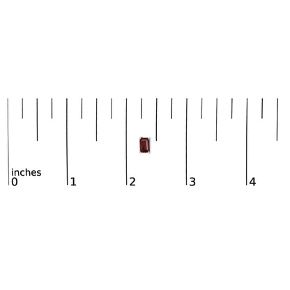 White metal stud earring with a single red emerald-shaped gemstone in a four-prong setting, shown on a scale from a top angle.