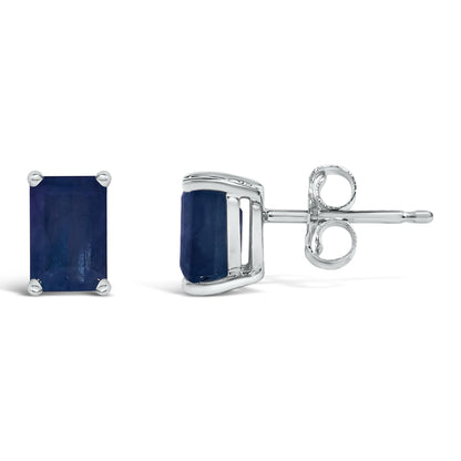 Pair of white metal stud earrings with blue emerald-shaped gemstones in a 4-prong setting, shown from front and side angles on a white background.