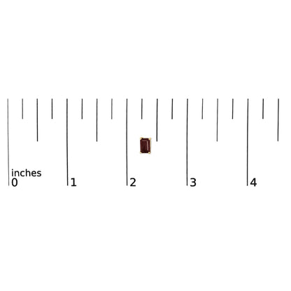 Single yellow metal earring with a red rectangular gemstone in a four-prong setting shown on a ruler scale from a top-down angle.