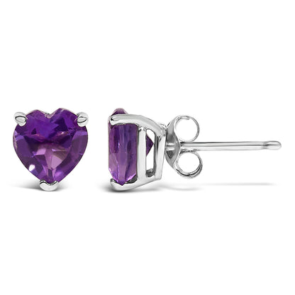 Close-up front and side view of white metal stud earrings each set with a heart-shaped purple gemstone in a three-prong setting, shown on a white background.