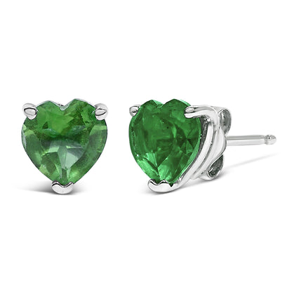 Pair of white metal stud earrings with heart-shaped green gemstones in three-prong settings, shown at a close-up angle.