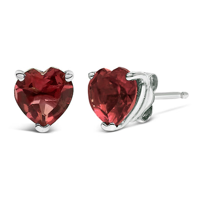 Close-up front and side angle of a pair of white metal stud earrings featuring heart-shaped red gemstones in three-prong settings.