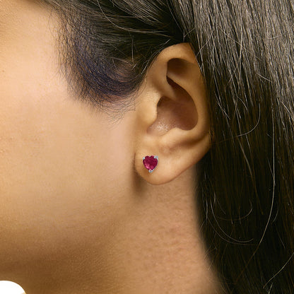 Close-up side view of a model wearing a white metal stud earring with a heart-shaped red gemstone in a three-prong setting.