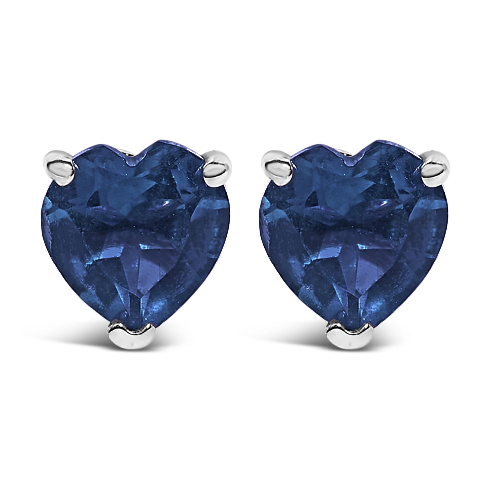 Front-facing close-up of a pair of white metal earrings each with a heart-shaped blue gemstone set in a three-prong setting.