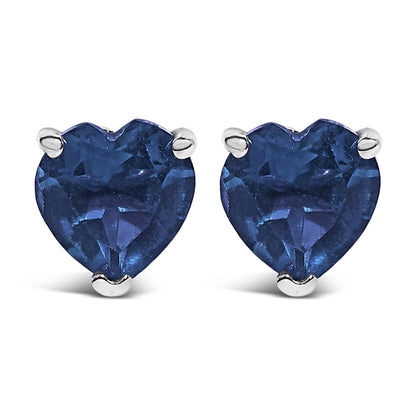 Front-facing close-up of a pair of white metal earrings each with a heart-shaped blue gemstone set in a three-prong setting.