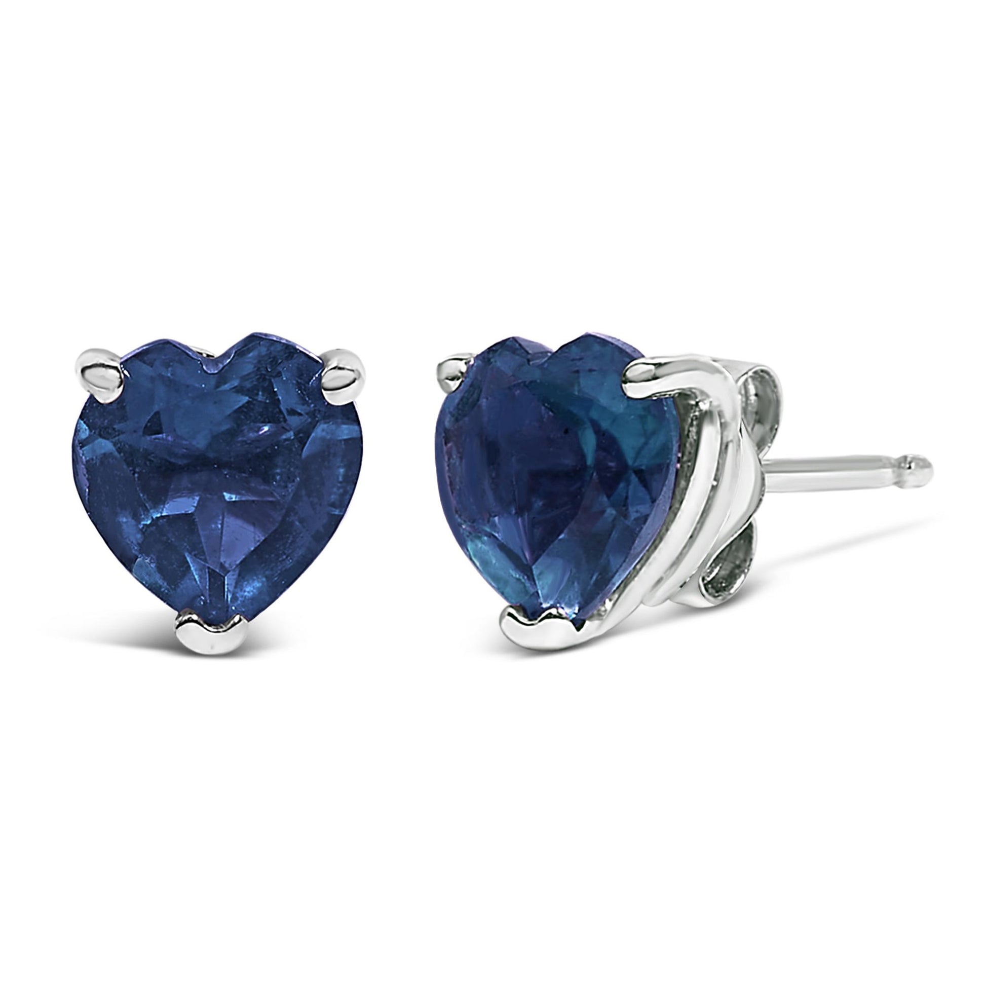 Pair of white metal stud earrings with heart-shaped blue gemstones set in three prongs, shown in a close-up front and side angle.
