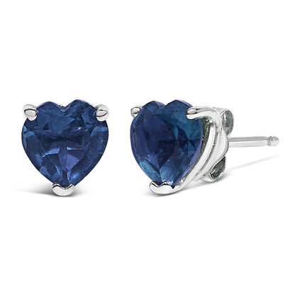 Pair of white metal stud earrings with heart-shaped blue gemstones set in three prongs, shown in a close-up front and side angle.