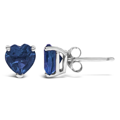 Pair of white metal stud earrings featuring heart-shaped blue gemstones set in three-prong settings, shown from front and side angles on a white background.
