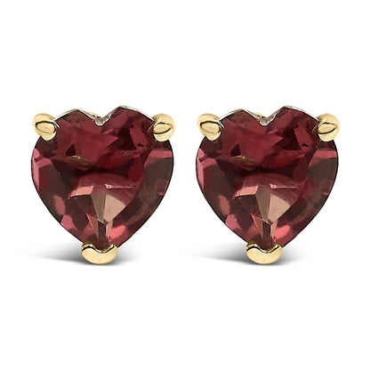Close-up front view of a pair of yellow metal stud earrings, each featuring a heart-shaped red gemstone set with three prongs.