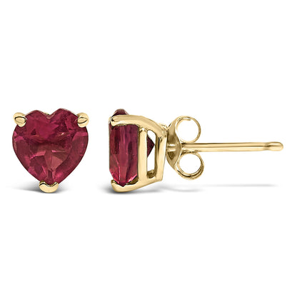 Close-up front and side view of yellow metal stud earrings with heart-shaped red gemstones in 3-prong settings.