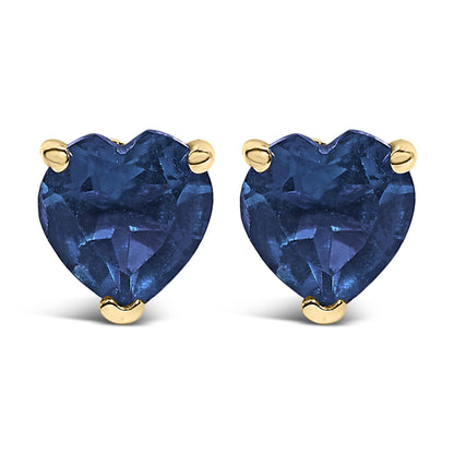 Close-up front view of yellow metal heart-shaped blue gemstone stud earrings with three-prong settings.