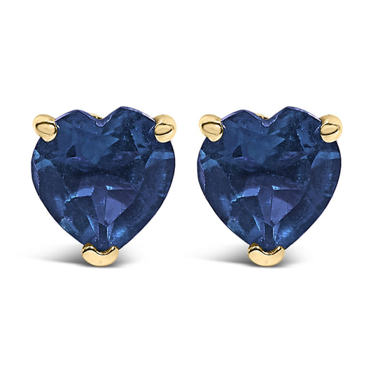 Close-up front view of yellow metal heart-shaped blue gemstone stud earrings with three-prong settings.