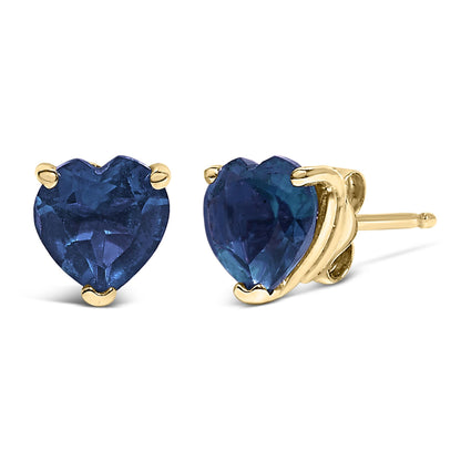 Close-up front and side view of yellow metal stud earrings with heart-shaped blue gemstones in a three-prong setting.