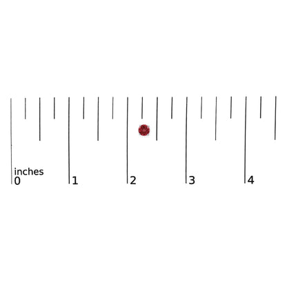 Close-up of a round red gemstone earring with four-prong setting placed on a ruler for scale.