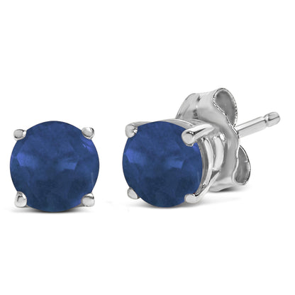 Pair of white metal stud earrings with round blue gemstones in four-prong settings, shown from a front and side angle on a white background.