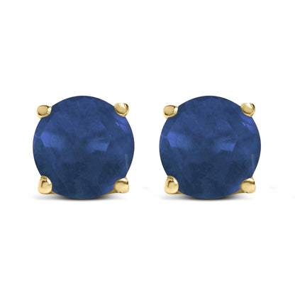 Front view of yellow metal stud earrings with round blue gemstones in four-prong settings.