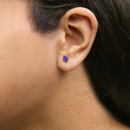 Close-up side view of a model's ear wearing a white metal earring with a pear-shaped purple gemstone in a three-prong setting.