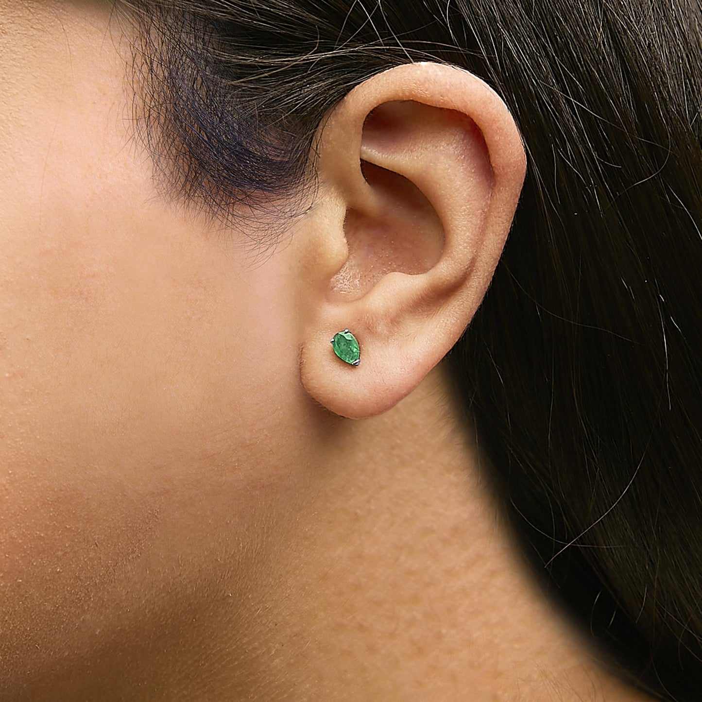 Close-up side view of a model wearing a white metal earring with a pear-shaped green gemstone in a three-prong setting.