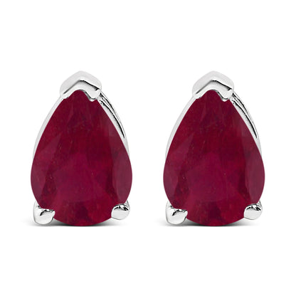 Close-up front view of a pair of white metal earrings, each featuring a pear-shaped red gemstone with a three-prong setting.