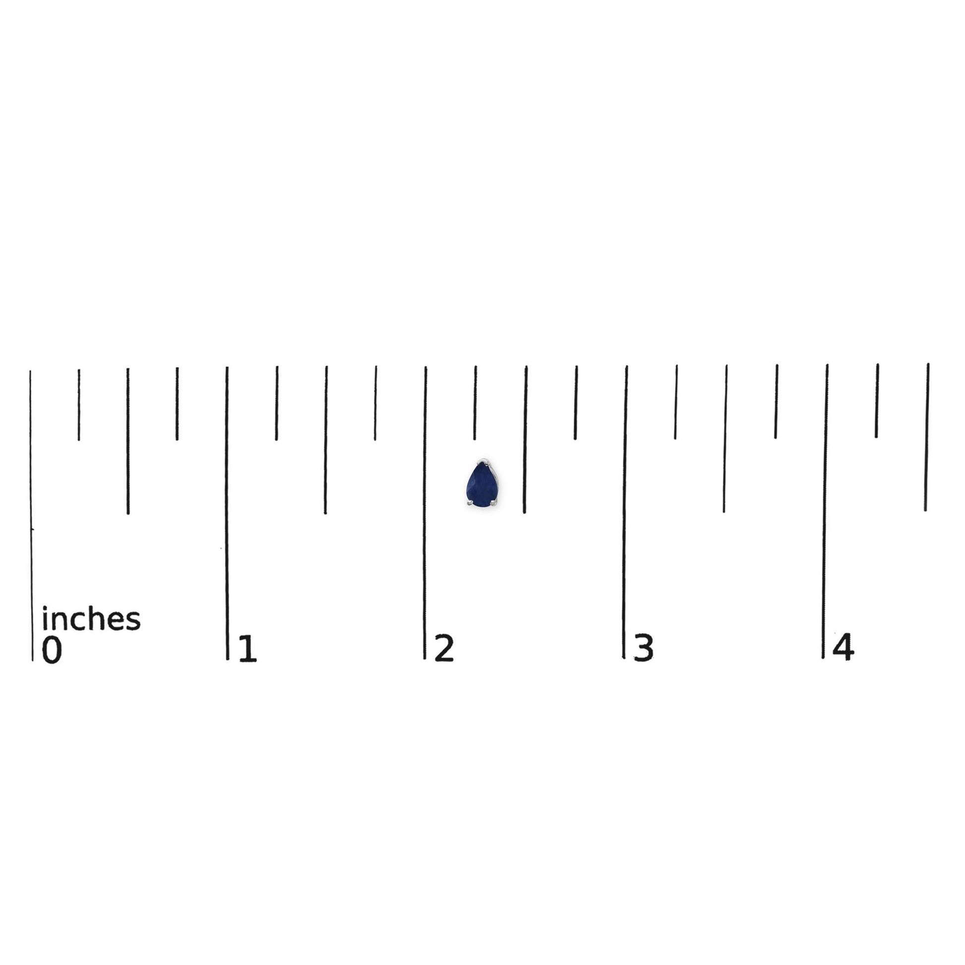 Close-up top view of a pair of white earrings each with a pear-shaped blue gemstone set with three prongs, shown on a ruler scale.