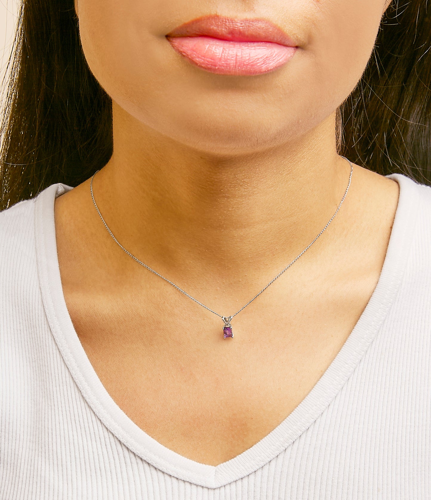 White metal necklace with a small emerald-shaped purple gemstone pendant shown worn on a model, front view.