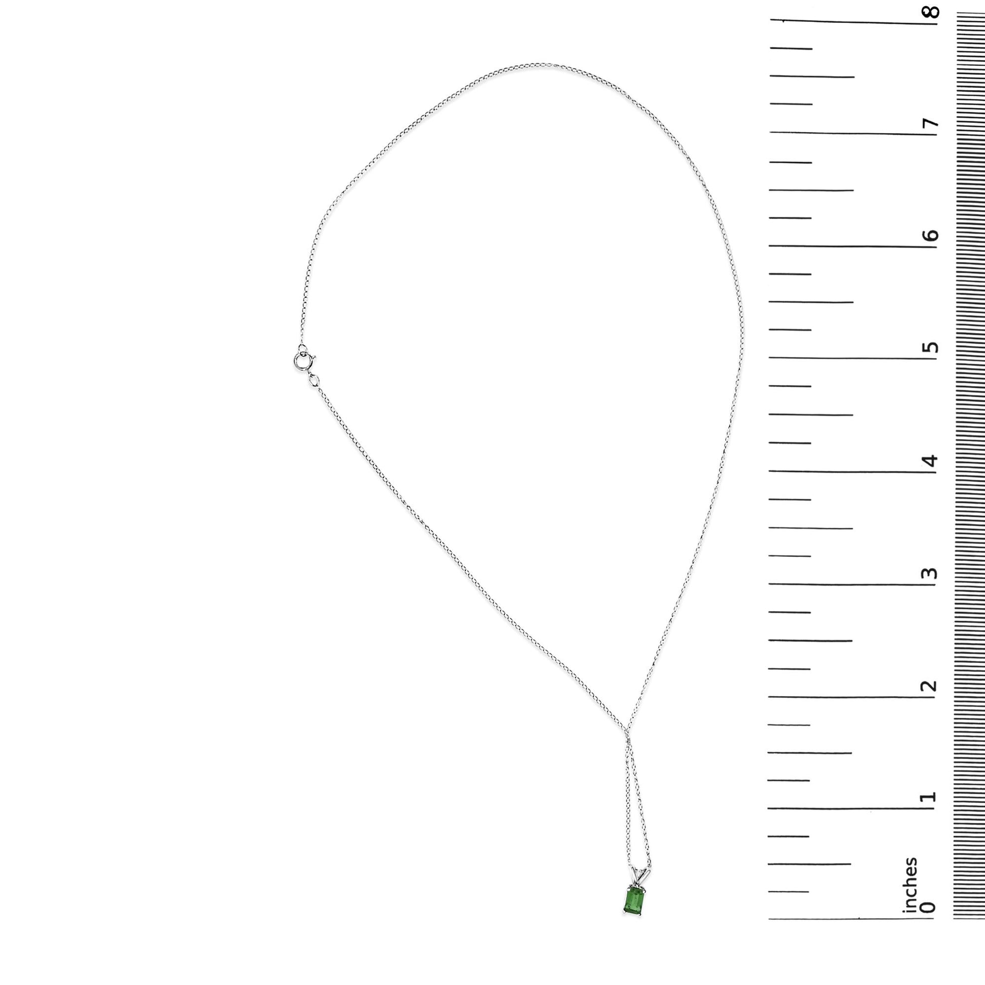 White necklace with a single rectangular green gemstone in a four-prong setting, shown on a scale, top-down angle.